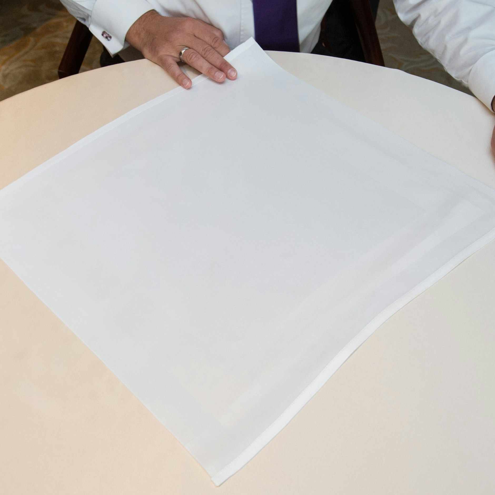 Schritt 1: Die Stoffserviette als Raute auf den Tisch legen. Diese zum Dreieck falten. Das heißt: Die untere Spitze auf die obere legen.