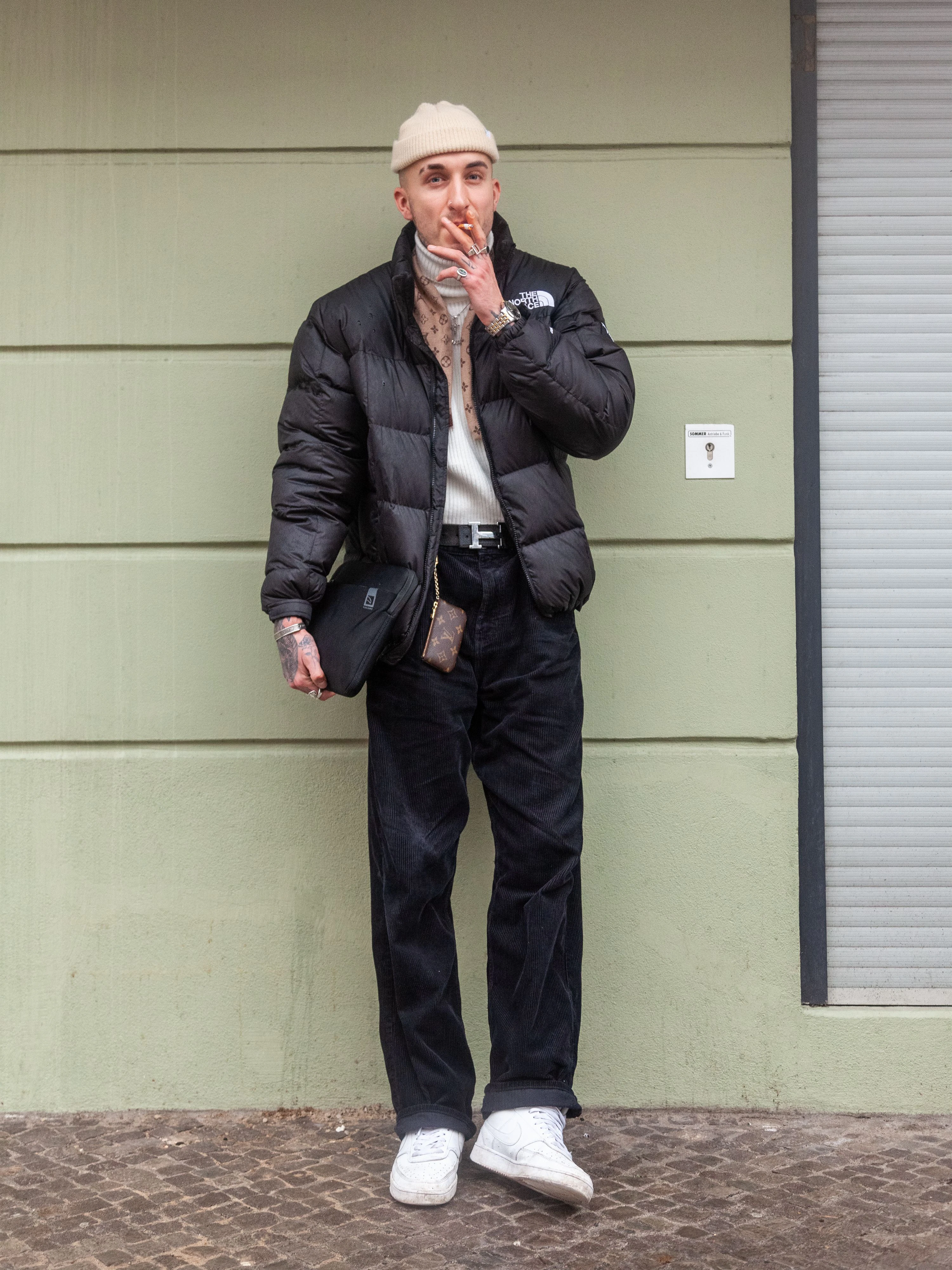Anito ist Tattoo-Artist, Designer und Skater. Sein Streetwear-Look überzeugt durch elegante Farbwahl: Puffer-Jacket von The North Face, Rollkragenpullover und Cordhose von Weekday. Schal und Zipper-Etui von Louis Vuitton, Gürtel von Hermès und die Sneakers: Jordan 1 von Nike.