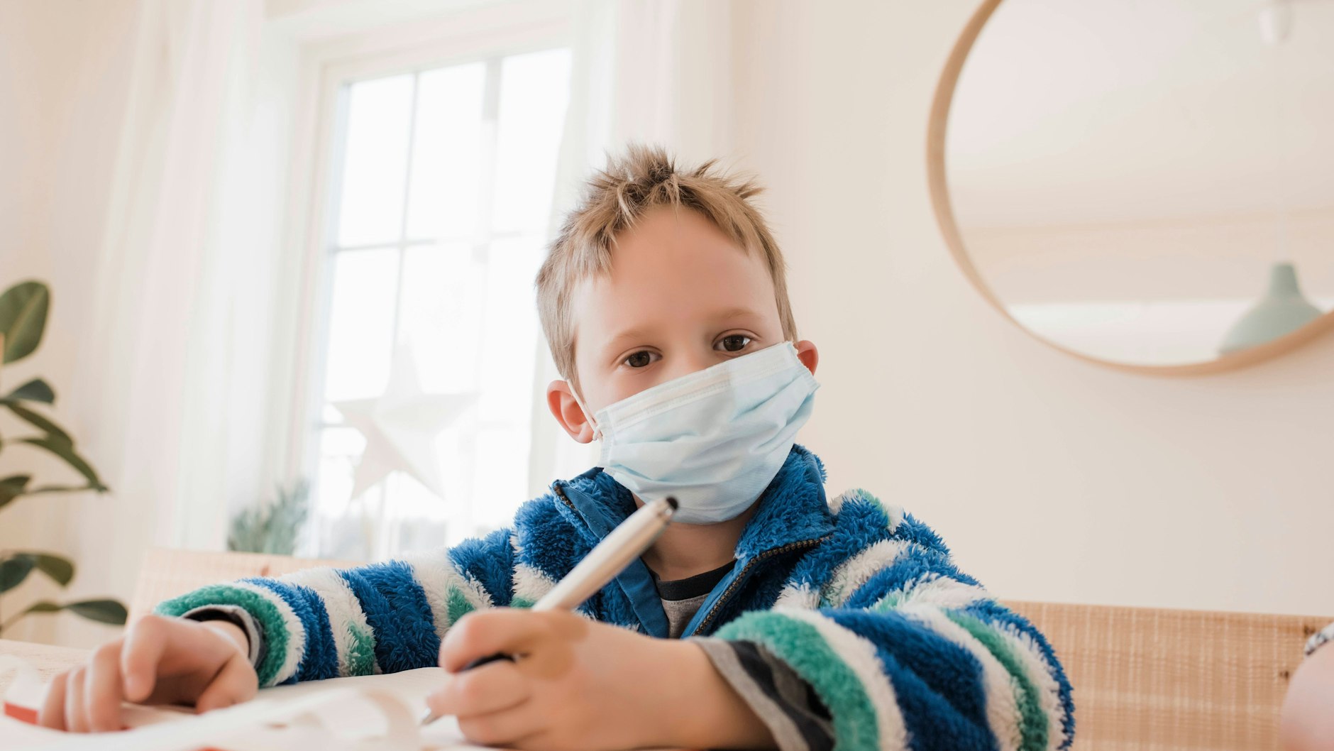 Ein Kind sitzt mit einer Maske zuhause.