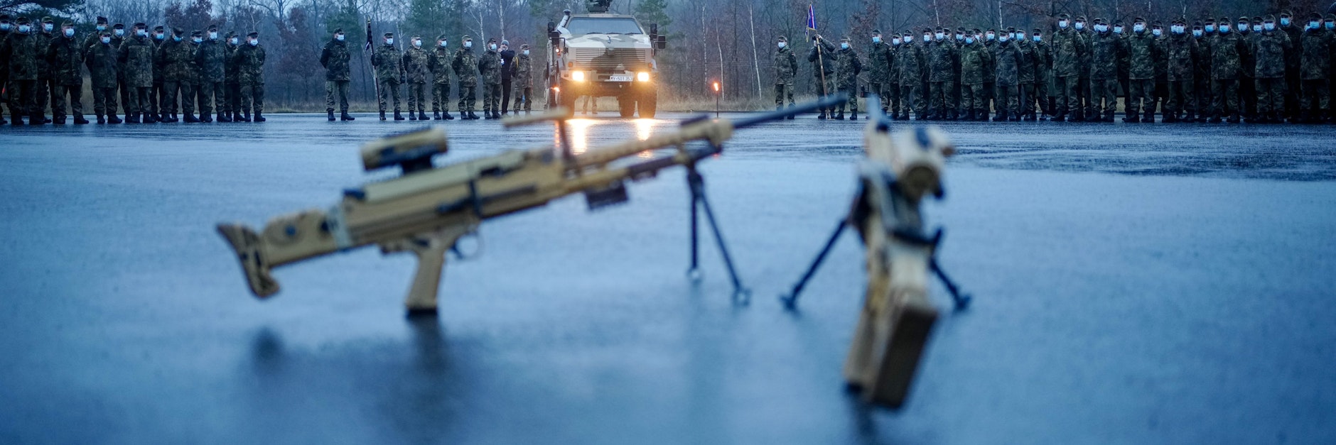 Soldaten auf einem Appellplatz hinter Maschinengewehren