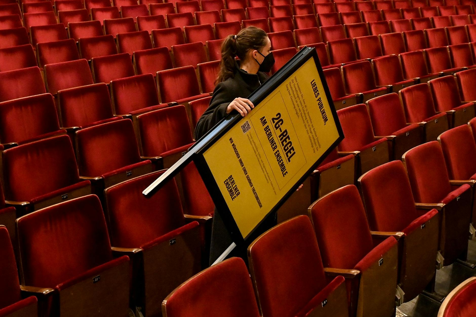 Eine Mitarbeiterin trägt einen Aufsteller mit dem Hinweis auf die 2G-Regel durch den Zuschauerraum des Berliner Ensemble