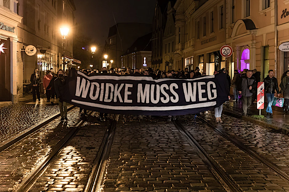 Mit einem Schild mit der Aufschrift „Woidke muss weg“ marschieren Demonstranten entlang des Cottbuser Altmarktes.
