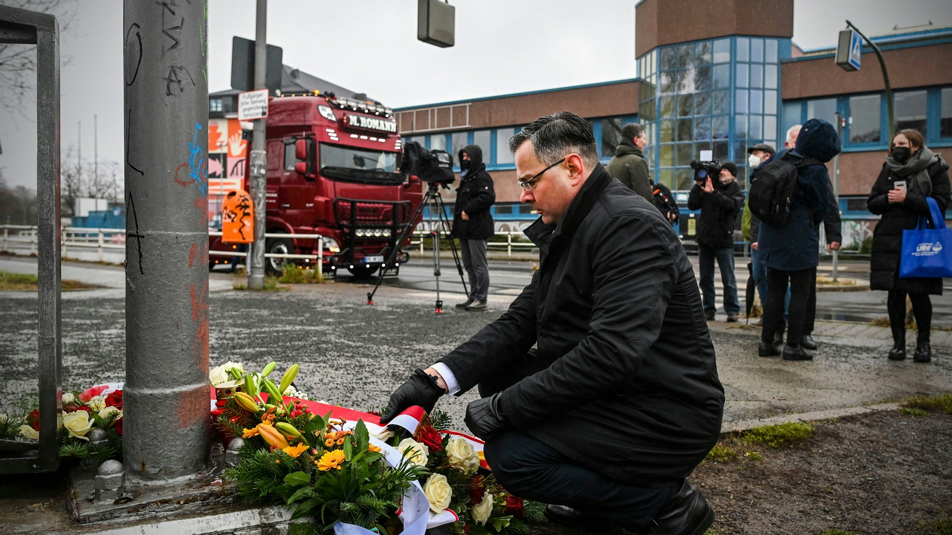 Der polnische Gesandte Pawel Gronow richtet die weiß-rote Schleife am Blumengebinde für Lukasz Urban.
