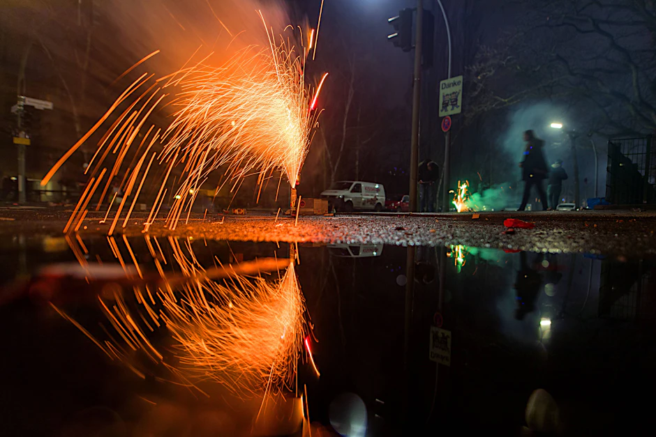 Bodenfeuerwerk zu Silvester spiegelt sich in einer Pfütze.