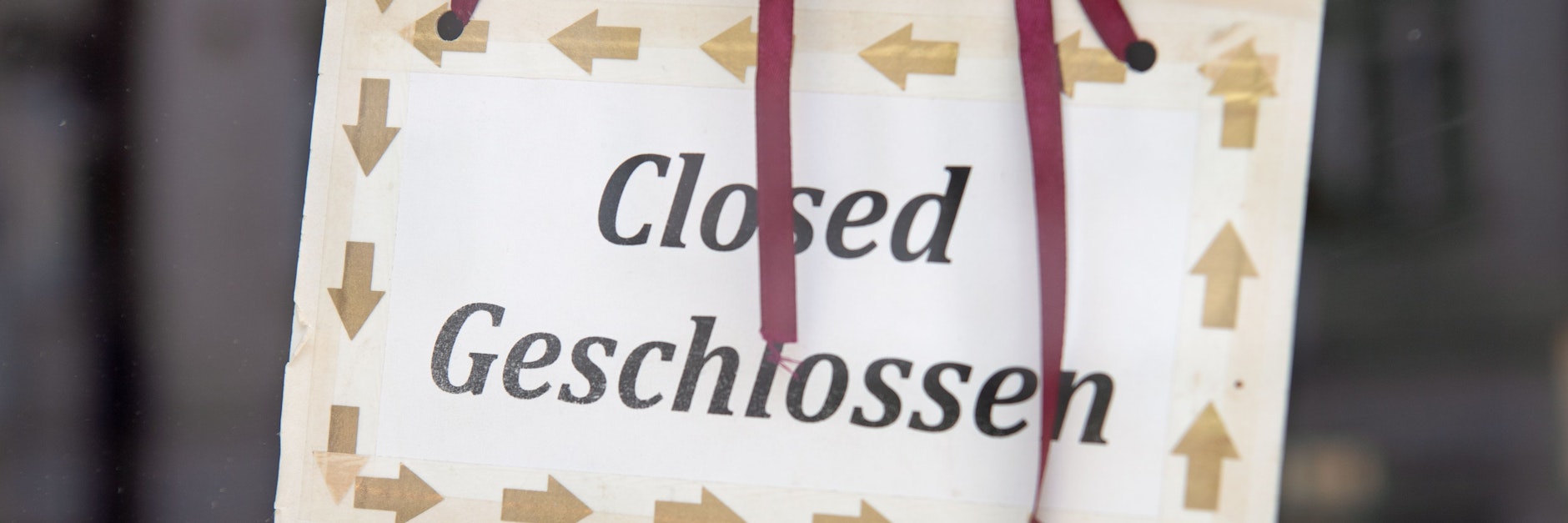 Ein Schild mit der Aufschrift „Closed“ und „Geschlossen“ hängt hinter einer Glasscheibe am Eingang eines Geschäftes in Berlin-Friedrichshain.