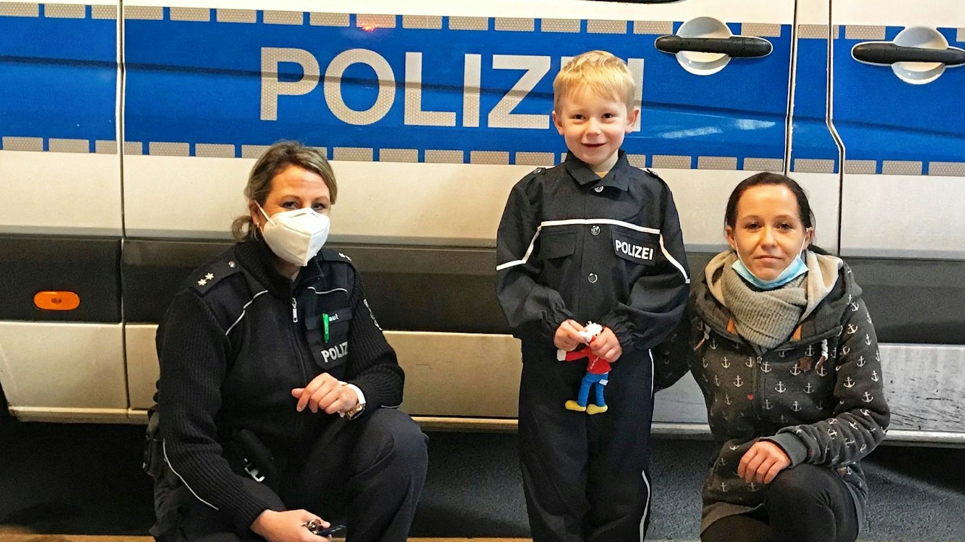 Der siebenjährige Ben mit einer Polizistin (links) und seiner Mama (rechts) vor einem Polizeiauto.