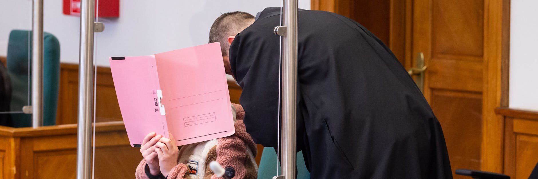 Die Angeklagte verdeckt während des Gespräches mit ihrem Anwalt ihr Gesicht mit einem Aktendeckel.