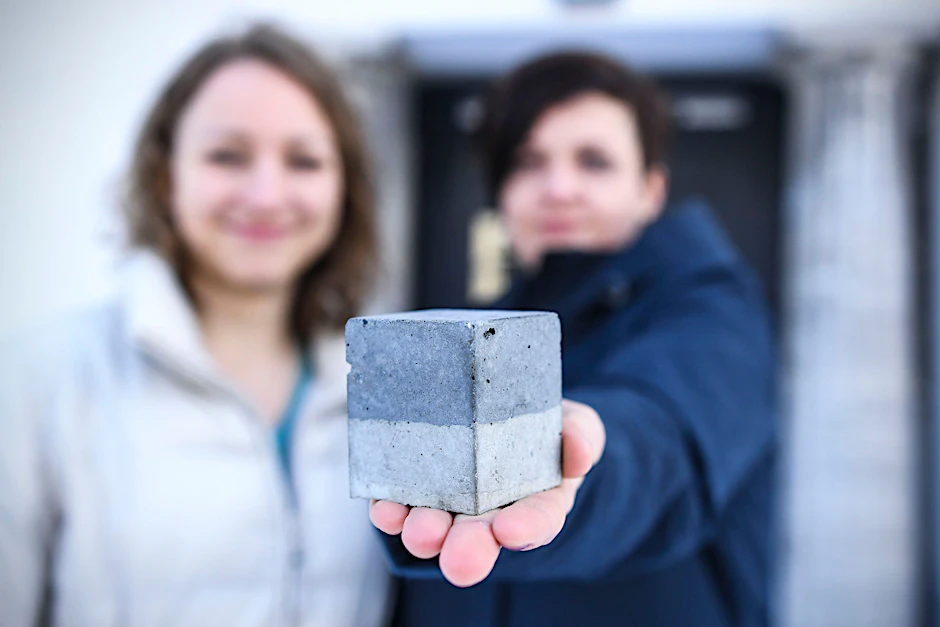 Die dunkle Hälfte des Würfels besteht aus einem Mix aus Pyrokohle und Zement. Die helle Hälfte besteht nur aus Zement. Mit ihrer Erfindung wollen Julia Roth (links) und Joanna Fatorelli die Bauindustrie nachhaltig verändern.&nbsp;