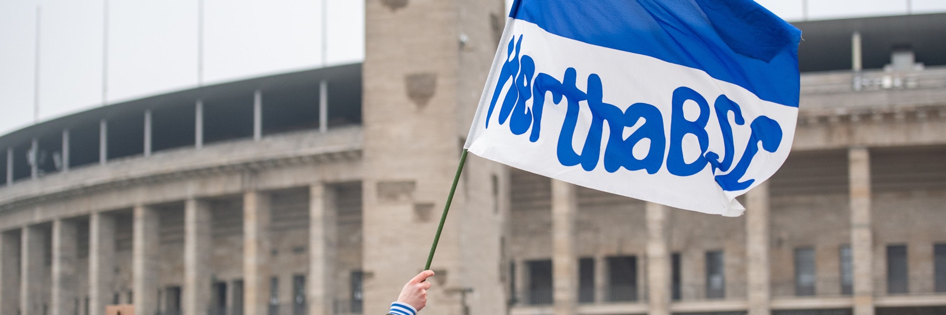 Ein Fußballfan schwenkt vor dem Olympiastadion mit Hertha BSC-Fahne.