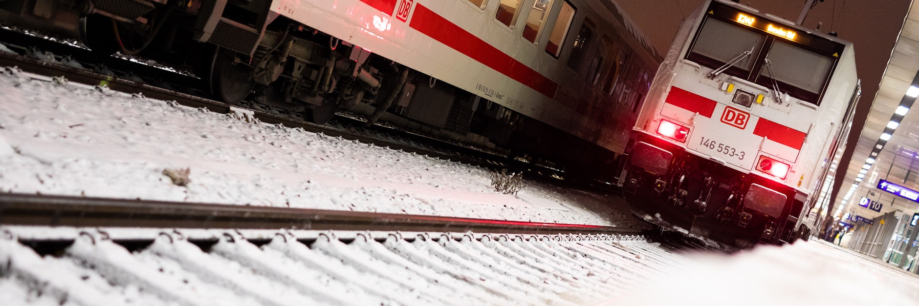 Züge der deutschen Bahn stehen in einem verschneiten Bahnhof.
