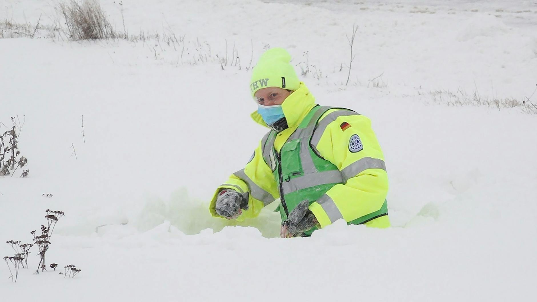 Ein Mann vom Technischen Hilfswerk THW steckt in einer hohen Schneewehe an der gesperrten Zufahrt zur Autobahn A7 fest. 