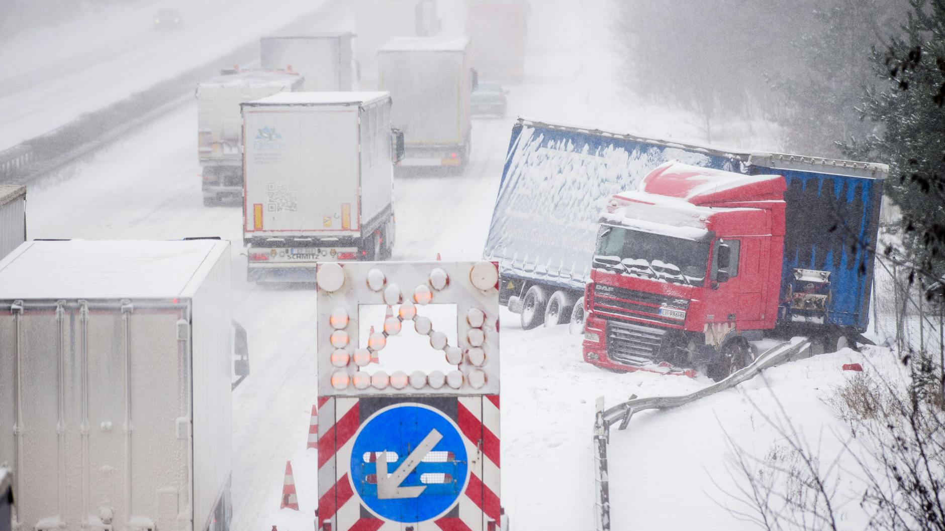 Möckern: Lastwagen rollen mit langsamer Fahrt auf der schneebedeckten A2 an einem in den Graben gerutschten Lkw vorbei. 