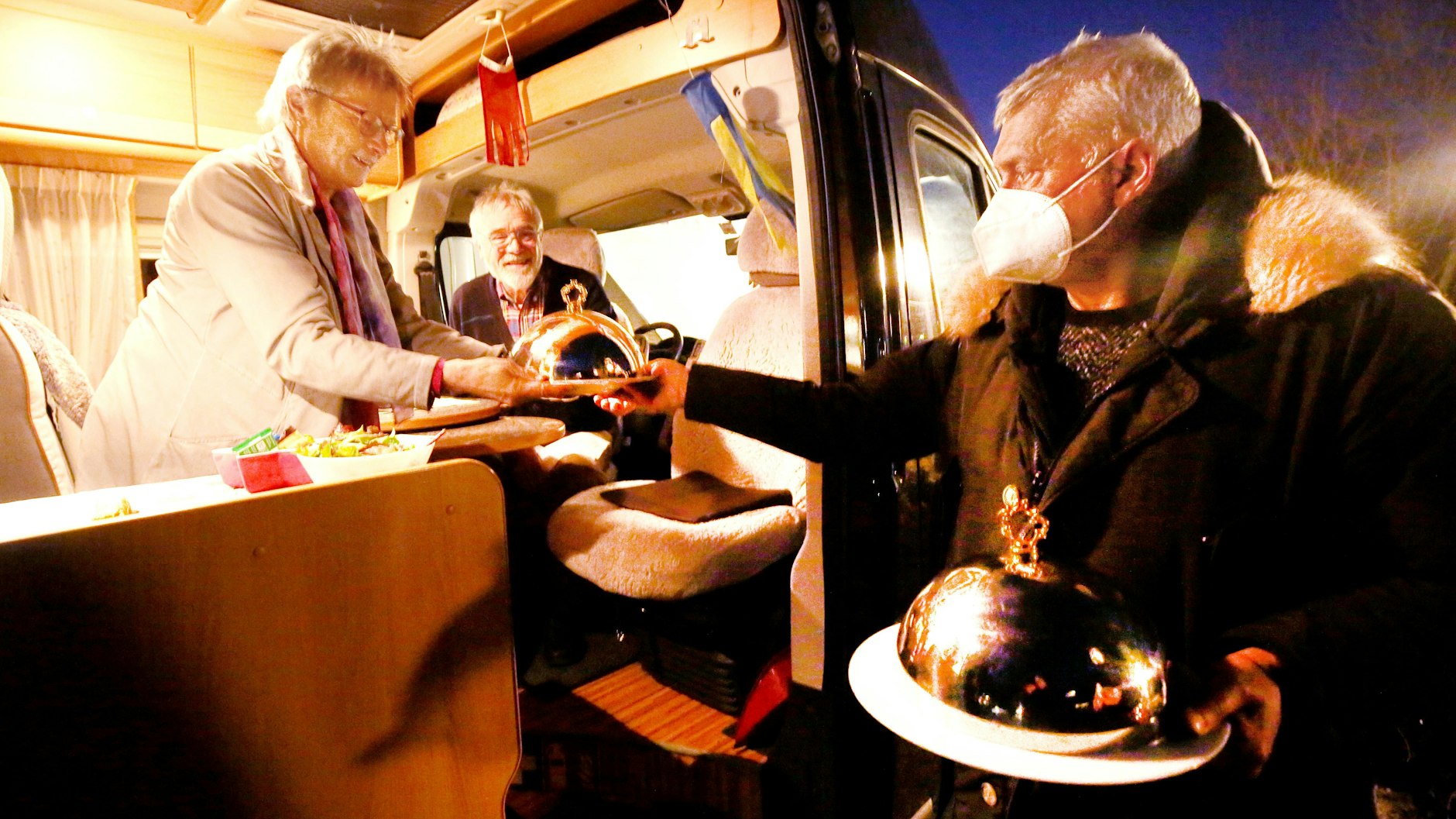 Hans-Werner Scherer vom „Bootshaus Ruhreck“ serviert seinen Kunden Dorothea und Hubert das bestellte Essen an ihrem Wohnmobil. Er darf es nicht betreten. Die Gäste es nicht verlassen.