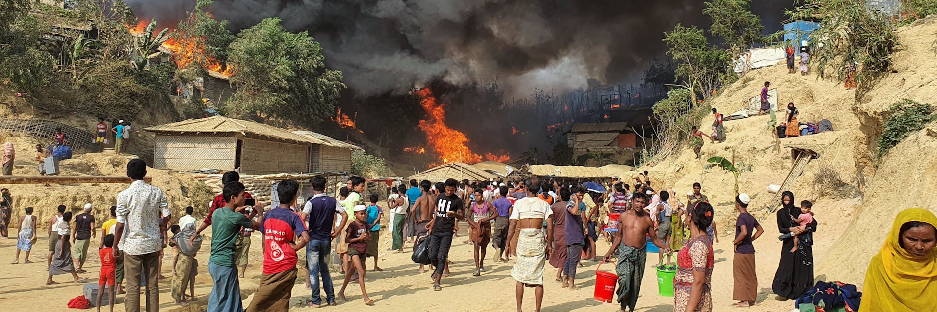 Zahlreiche Menschen betrachten den Rauch, der über dem in Flammen stehenden Lager aufsteigt.