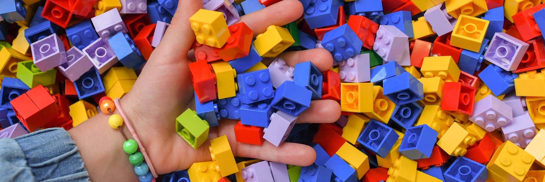 Ein Mädchen greift in eine Kiste voller Lego-Steine. Viele verbinden mit Lego eine kreative, bunte Spielwelt für Kinder und Jugendliche. 