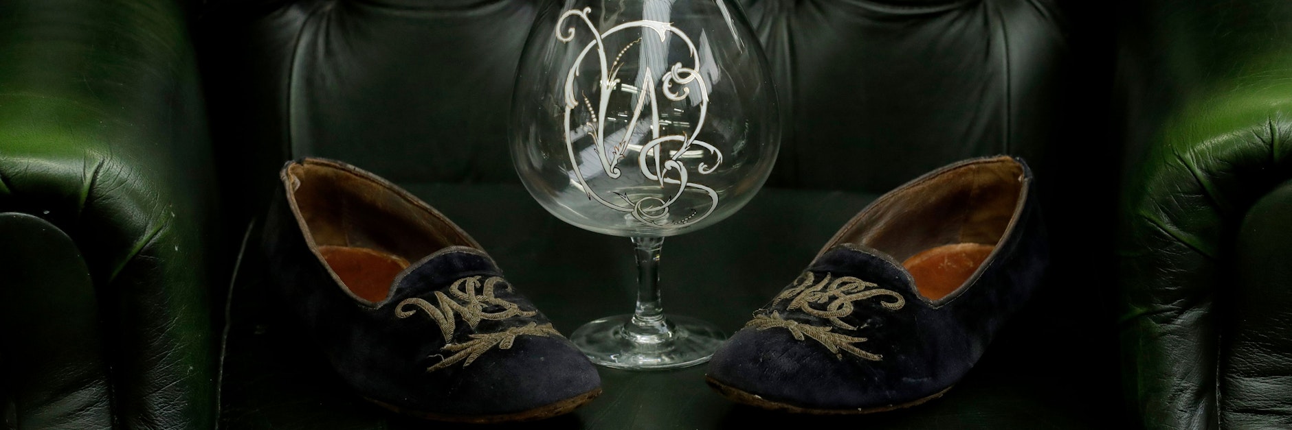 Ein Paar Samtslipper aus dem Zweiten Weltkrieg, die mit einem Monogramm von Großbritanniens ehemaligen Premierminister Winston Churchill versehen sind, werden auf einem Ledersessel ausgestellt.