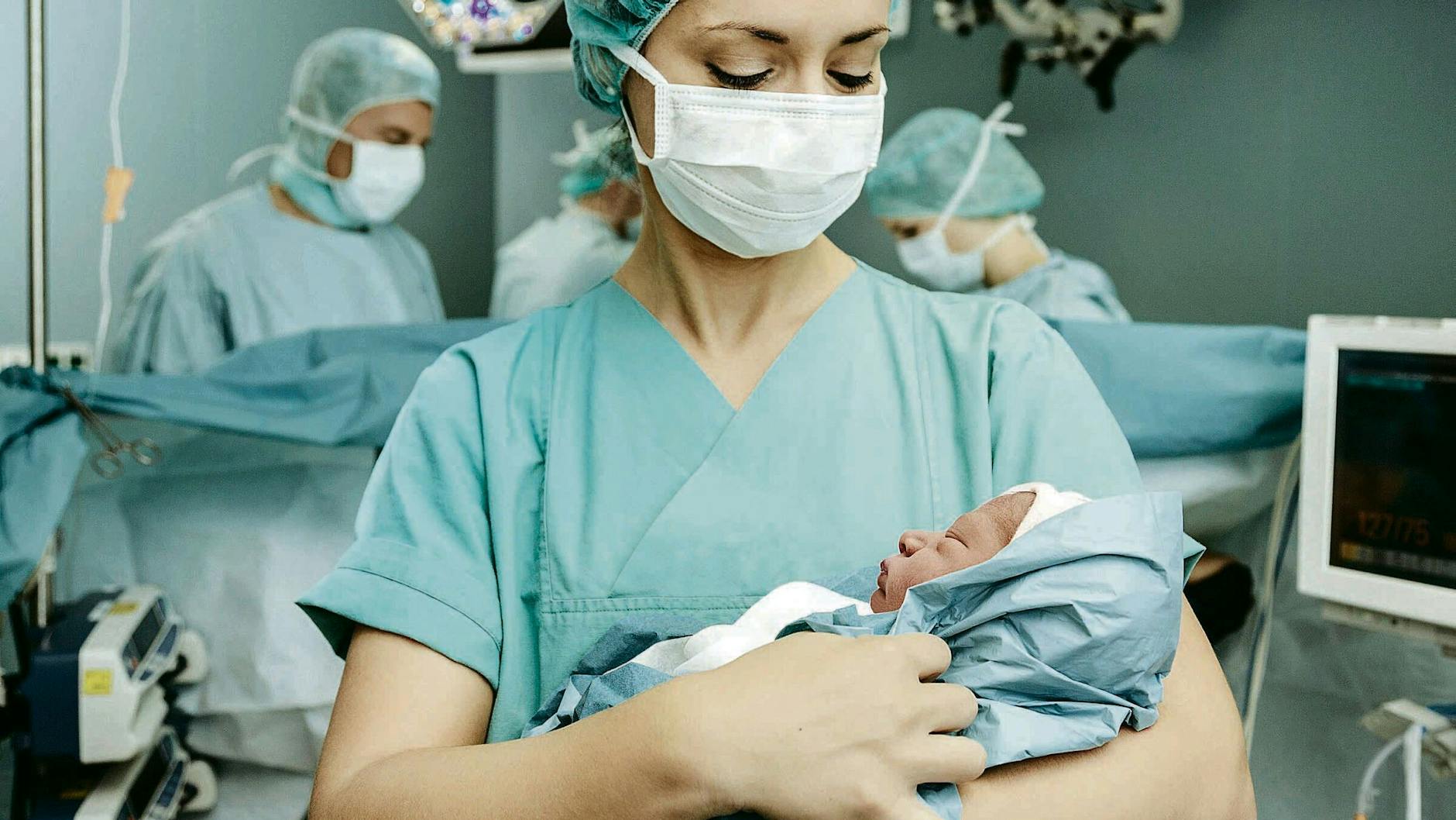 Eine Krankenpflegerin hält ein Neugeborenes im Operationssaal.
