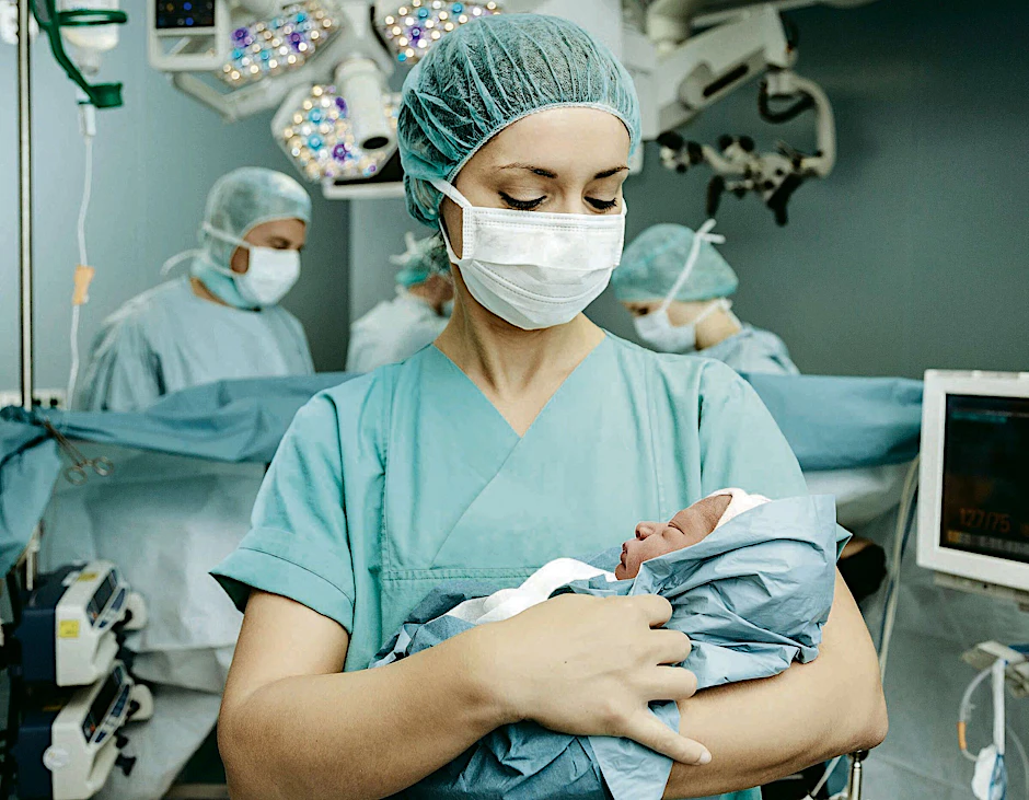 Eine Krankenpflegerin hält ein Neugeborenes im Operationssaal.