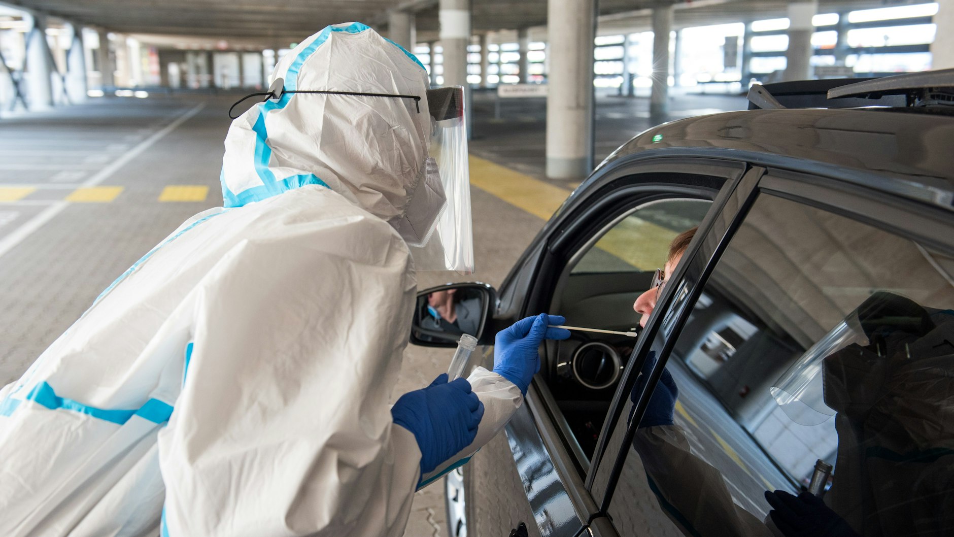 Eine Mitarbeiterin eines Drive-Through-Corona-Testzentrums nimmt einen Abstrich bei einer Autofahrerin. 