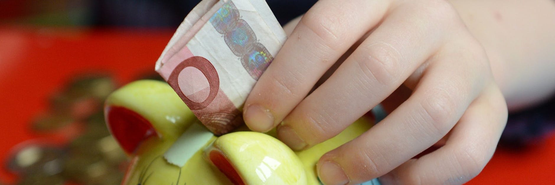Ein Junge steckt Geld in sein Sparschwein. 