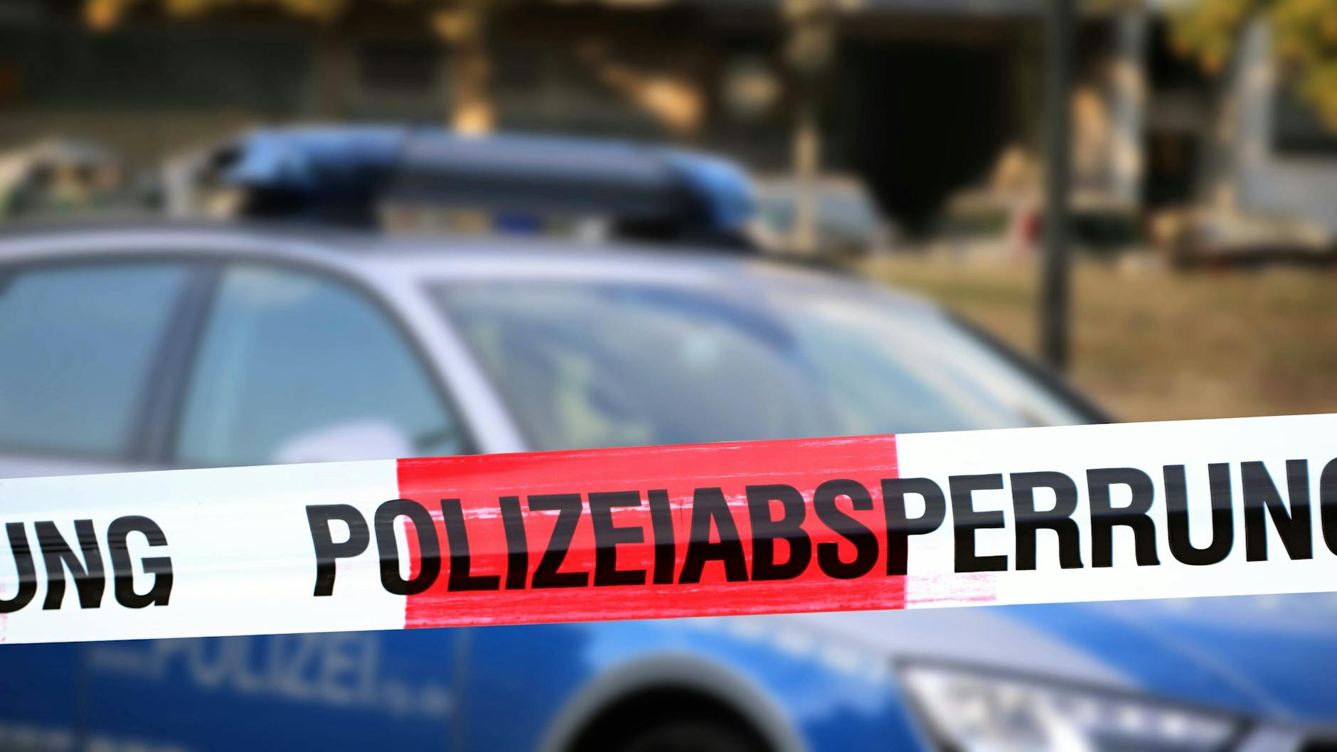 Ein Einsatzwagen der Polizei steht hinter einer Absperrung (Symbolbild).