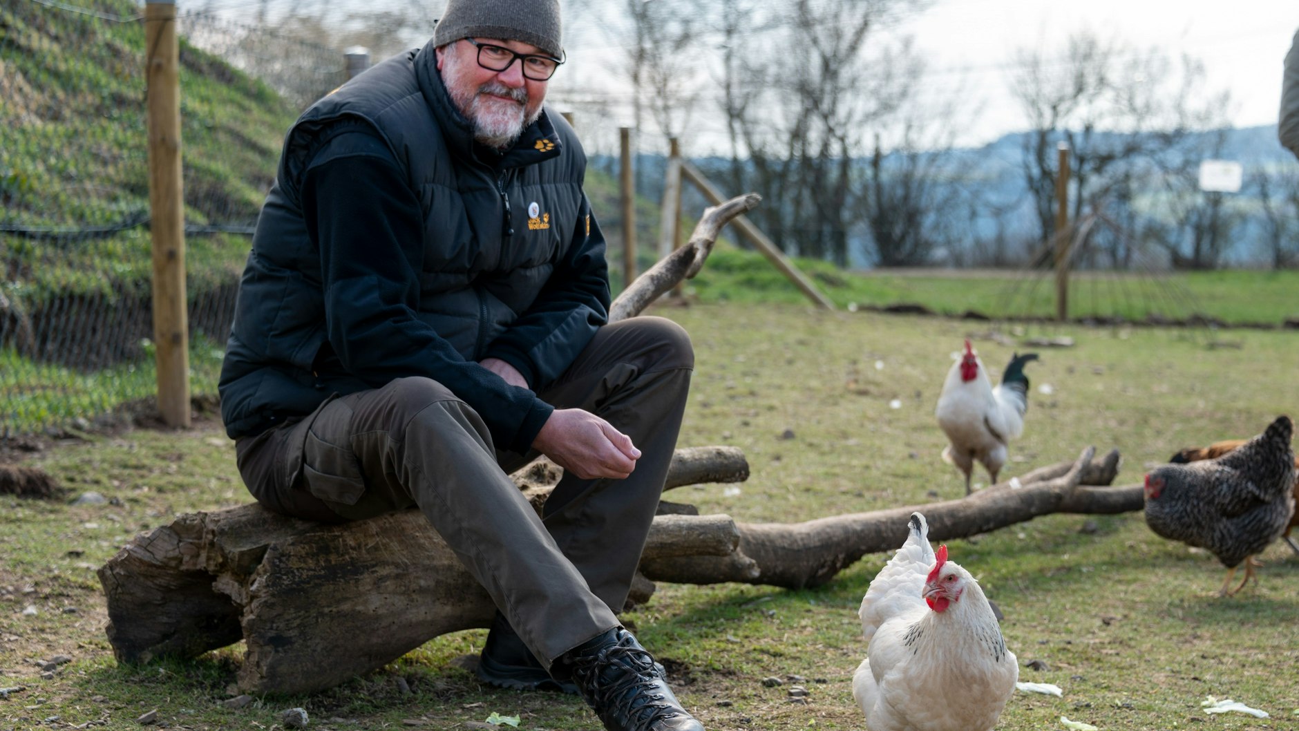 Initiator und Mitglied der Hühnergruppe Jochen Dostal sitzt im Gehege, während die Hühner frei um ihn herumlaufen.