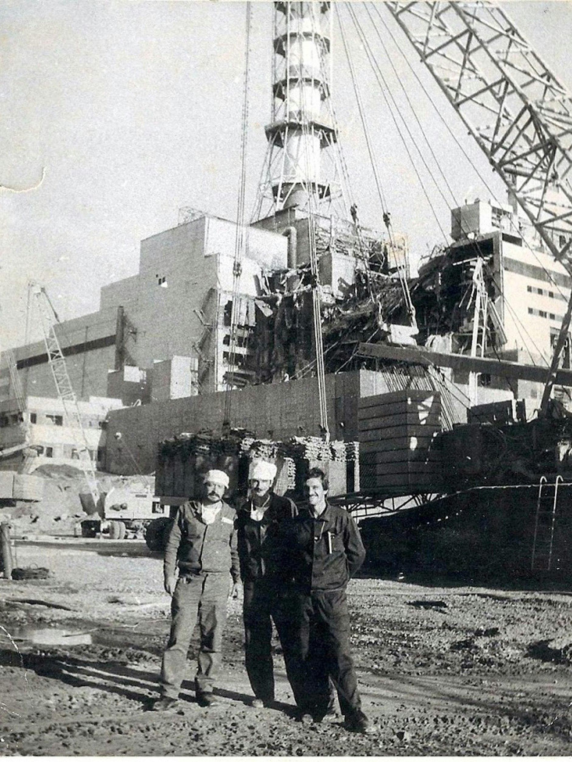 Die Aufnahme, die um den 25. August 1986 entstanden ist, zeigt die erste, gut 17 Meter hohe Kaskade des ersten Betonsarkophags am explodierten Block vier des Atomkraftwerks Tschernobyl. Davor steht Ilja Suslow (r.) mit zwei Kollegen für ein Erinnerungsfoto.&nbsp;