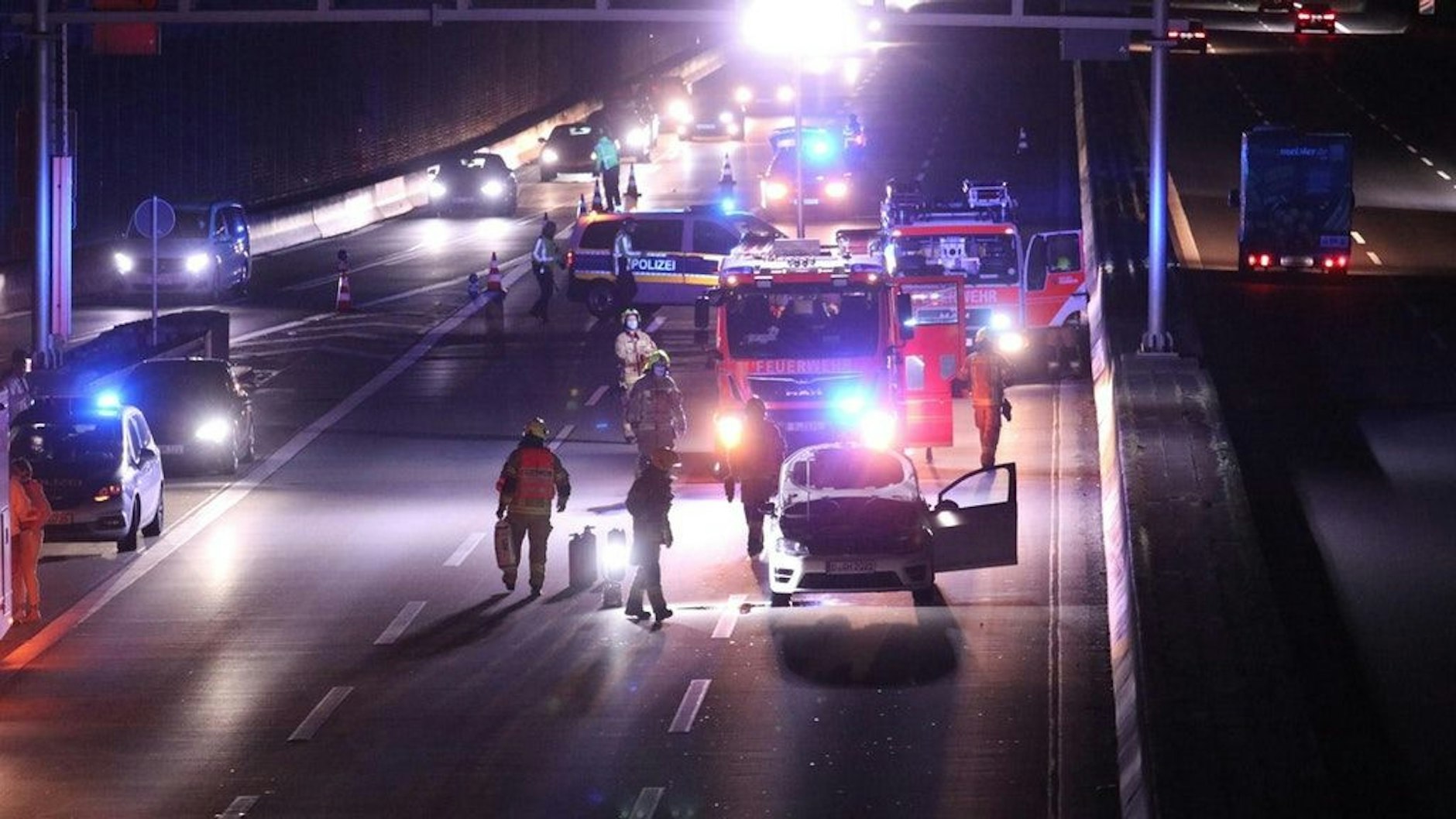 Einsatzkräfte der Berliner Feuerwehr stehe an dem gelöschten Fahrzeug.