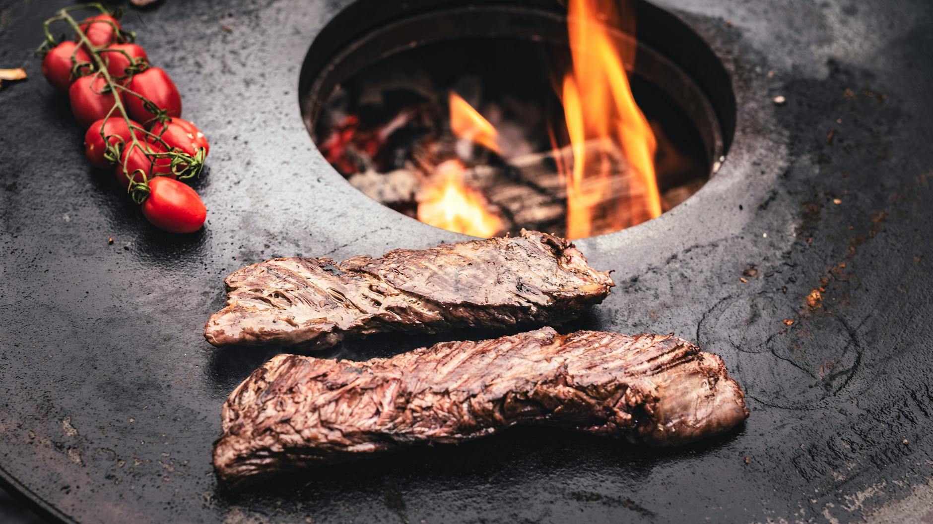 Die Feuerplatte - hier mit Rispentomaten und Nierenzapfen - gibt es als gusseisernen Aufsatz für den Kugelgrill. 