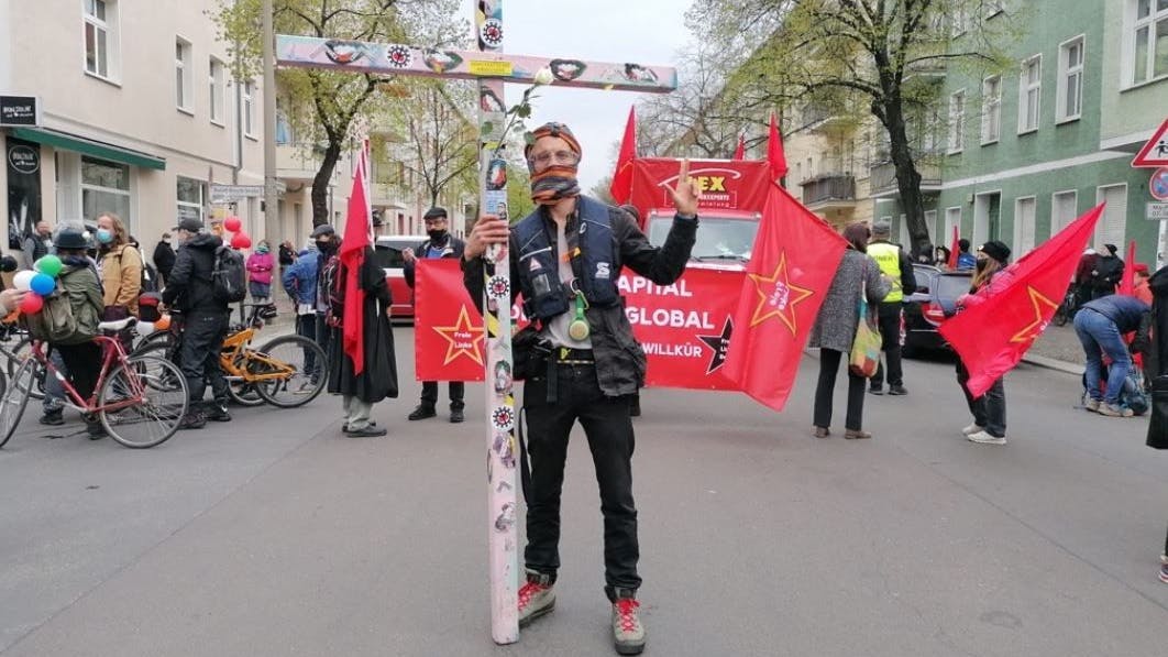 Lichtenberg: Ein vermummter Mann hält ein selbst gebasteltes Kreuz hoch. Darauf steht: „demokratischer Widerstand“.