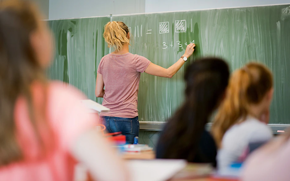 Eine junge Lehrerin schreibt an eine Schultafel im Mathematikunterricht einer 8. Klasse.