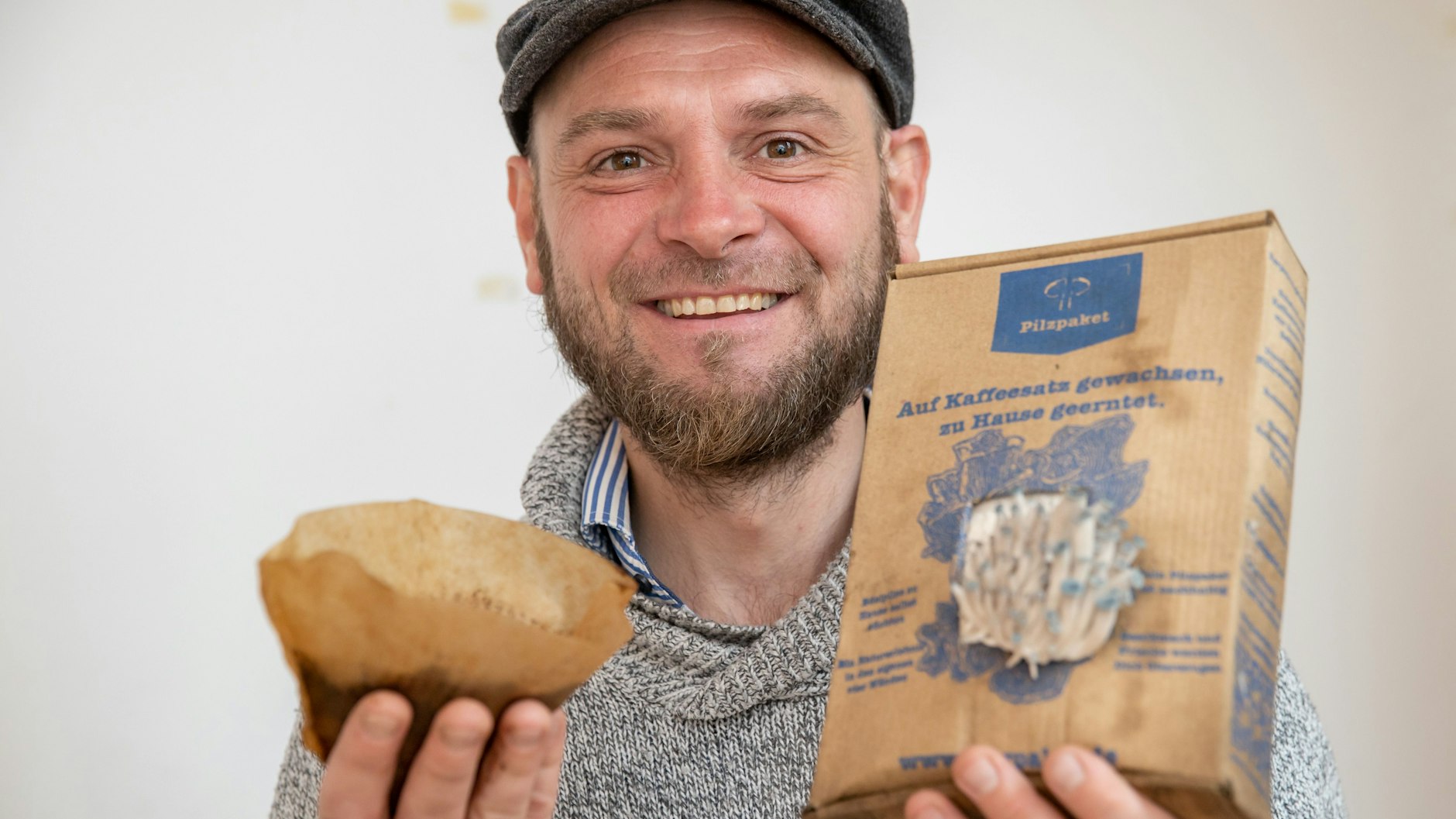 Ralph Haydl hält einen Kaffee-Filter mit altem Kaffeesatz in der einen sowie ein Pilzzuchtset mit Taubenblauen Austernseitlingen in der anderen Hand.
