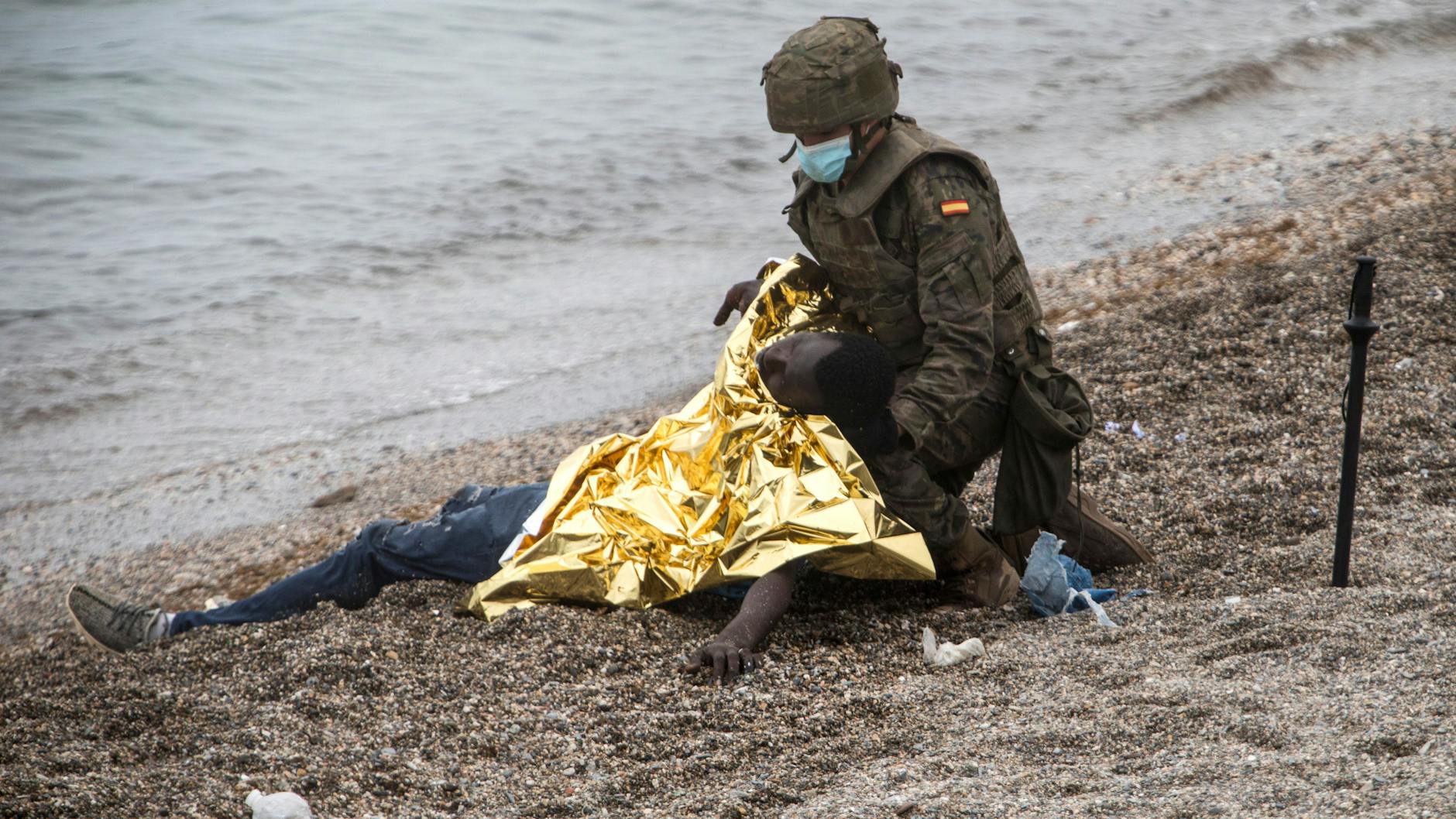 Ein spanischer Soldat bedeckt einen durchnässten, frierenden Flüchtling mit einer Rettungsdecke.