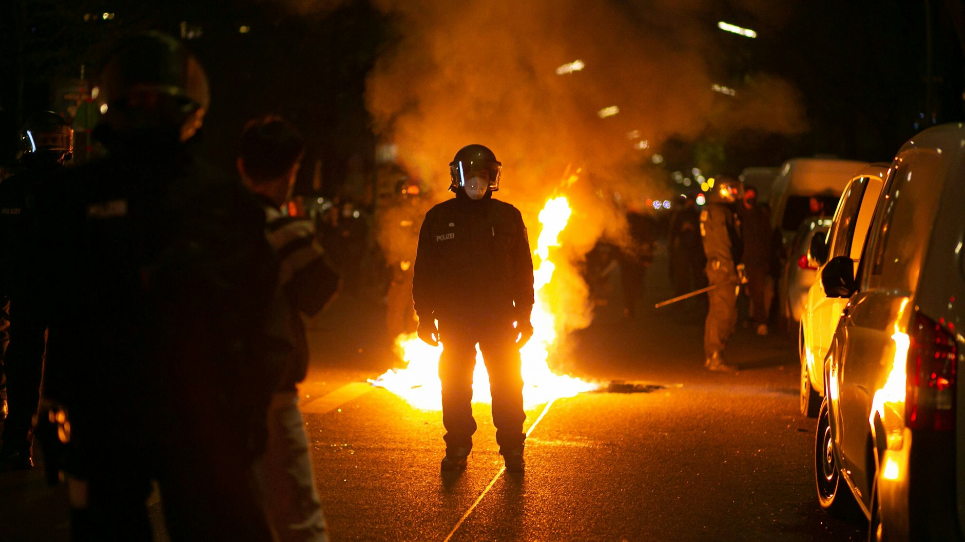 Ein Polizist steht am 1. Mai in Berlin-Neukölln vor einer brennenden Barrikade.