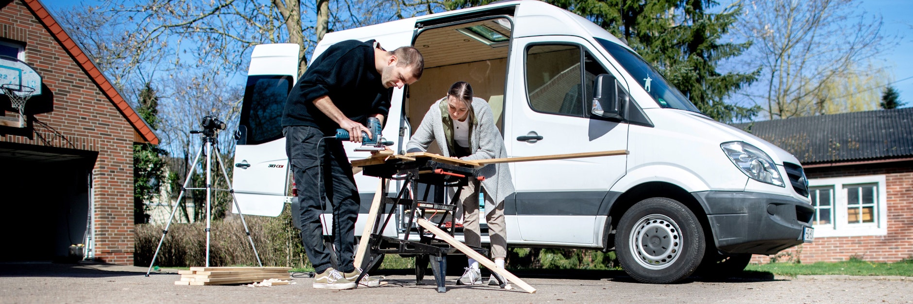 Greta Thomas und Hannes Wehrmann sägen Holz vor ihrem Mercedes-Benz Sprinter, den das Paar in Eigenarbeit zu einem Campervan umbaut.&nbsp;