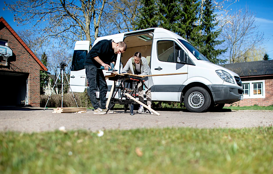 Greta Thomas und Hannes Wehrmann sägen Holz vor ihrem Mercedes-Benz Sprinter, den das Paar in Eigenarbeit zu einem Campervan umbaut.&nbsp;