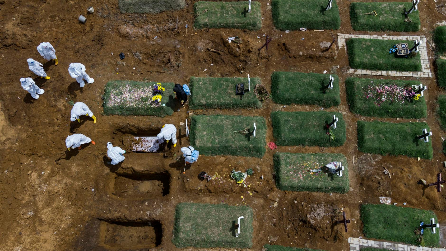 Indonesische Arbeiter in Schutzausrüstung bedecken einen Sarg mit dem Leichnam eines Corona-Toten auf einem speziell für Corona-Opfer vorgesehenen Friedhof mit Erde.