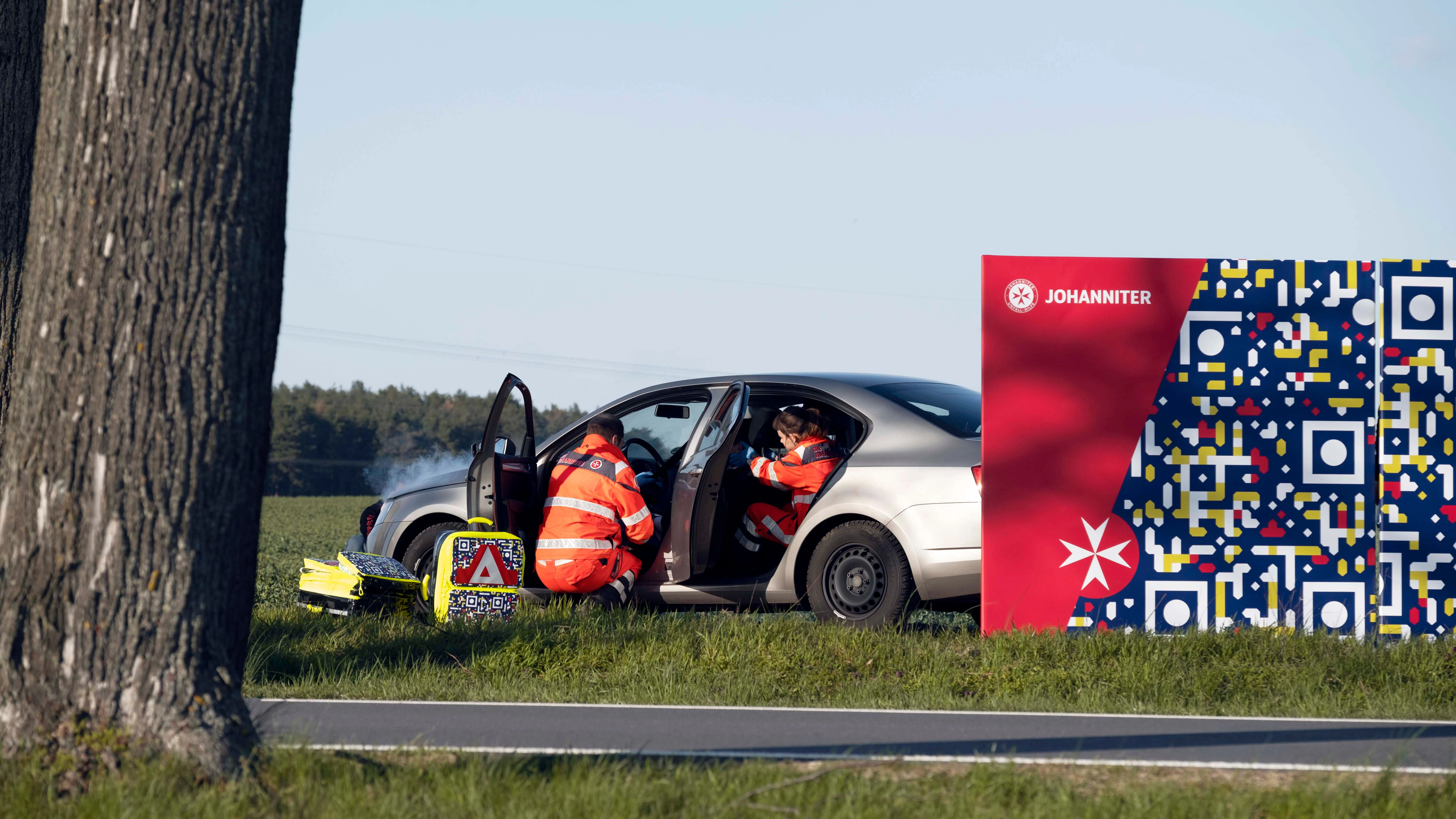 Neben einer gestellten Unfallszene der Johanniter-Unfall-Hilfe ist eine Stellwand mit einem QR-Code zu sehen, der die Botschaft „Gaffen tötet“ enthält.