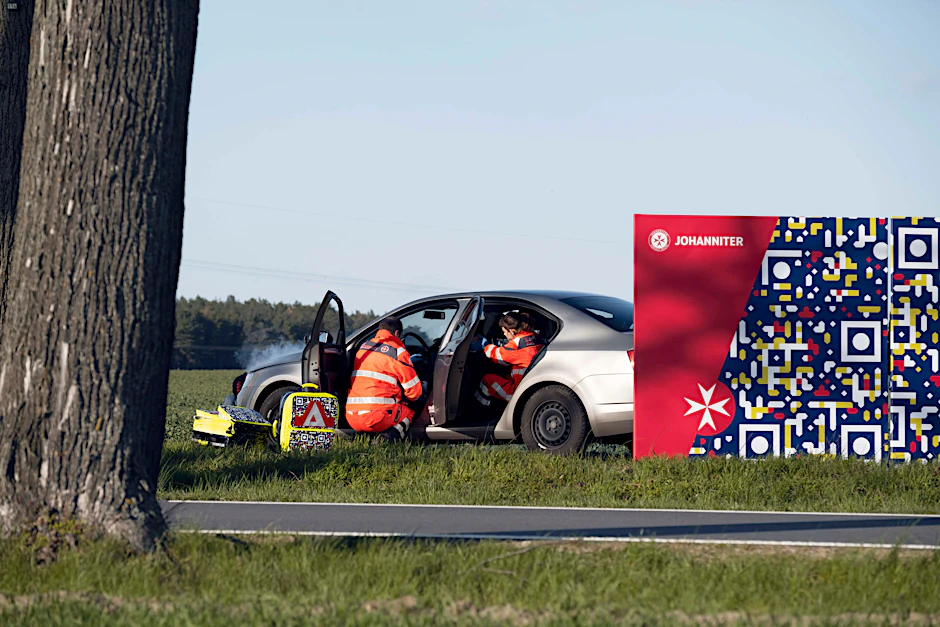 In einer gestellten Szene wird eine Unfallsituation mit einem Smartphone fotografiert. Das Handy erkennt den QR-Code.