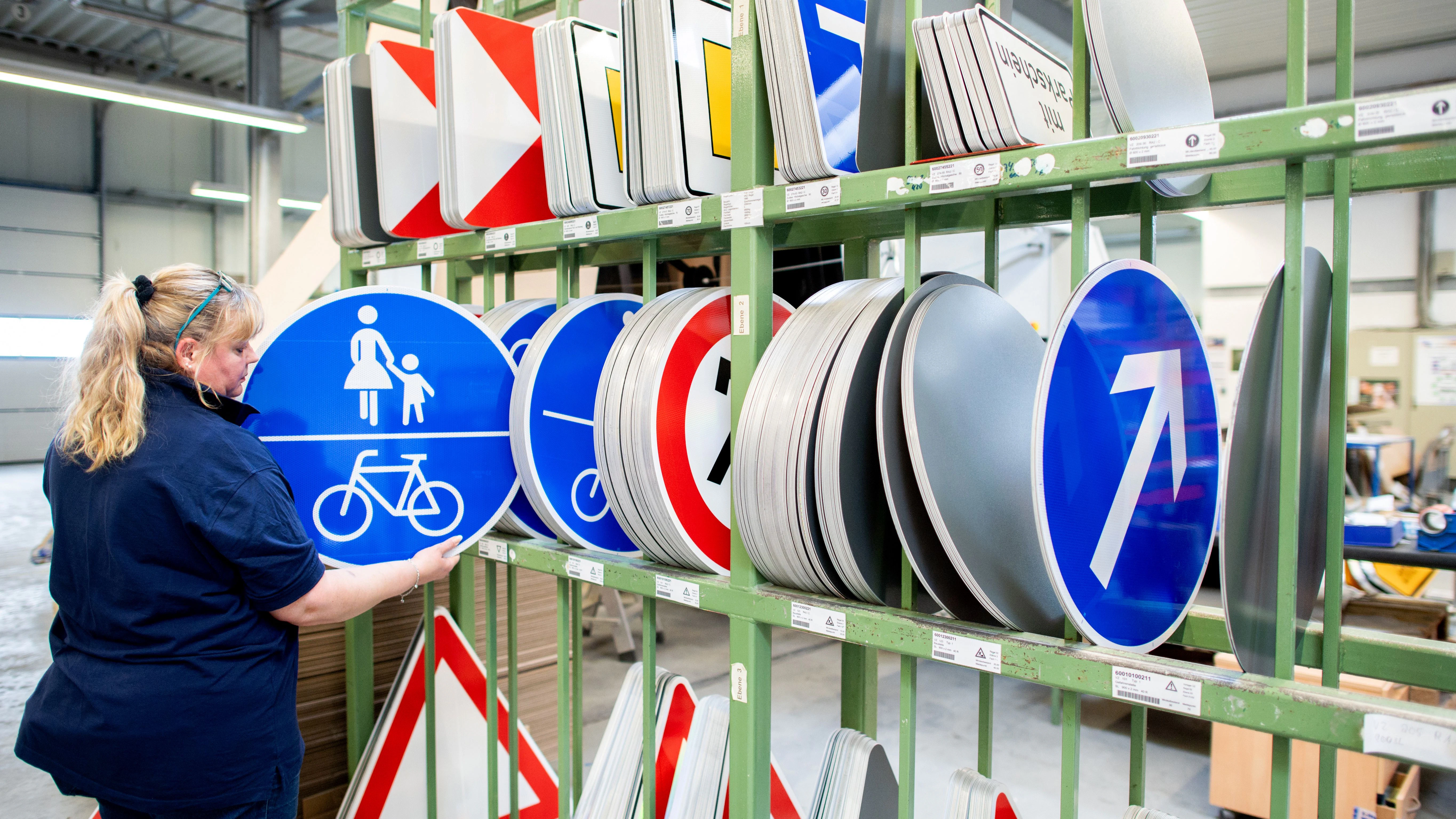 Mitarbeiterin Kirstin Geide entnimmt ein blaues Verkehrsschild für einen gemeinsamen Fuß- und Radweg aus einem Regal.&nbsp;