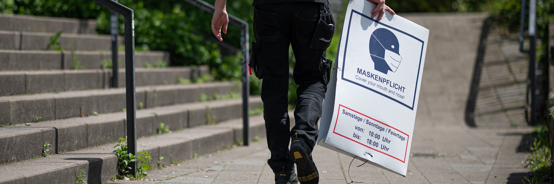 Ein Mann&nbsp; bringt ein abgehängtes Hinweisschild zur Maskenpflicht zu seinem Fahrzeug. Laut den vom Senat beschlossenen Lockerungen der Corona-Einschränkungen fällt die abstandsunabhängige Maskenpflicht in den Grünanlagen entlang von Alster und Elbe seit dem 22. Mai 2021 weg.&nbsp;