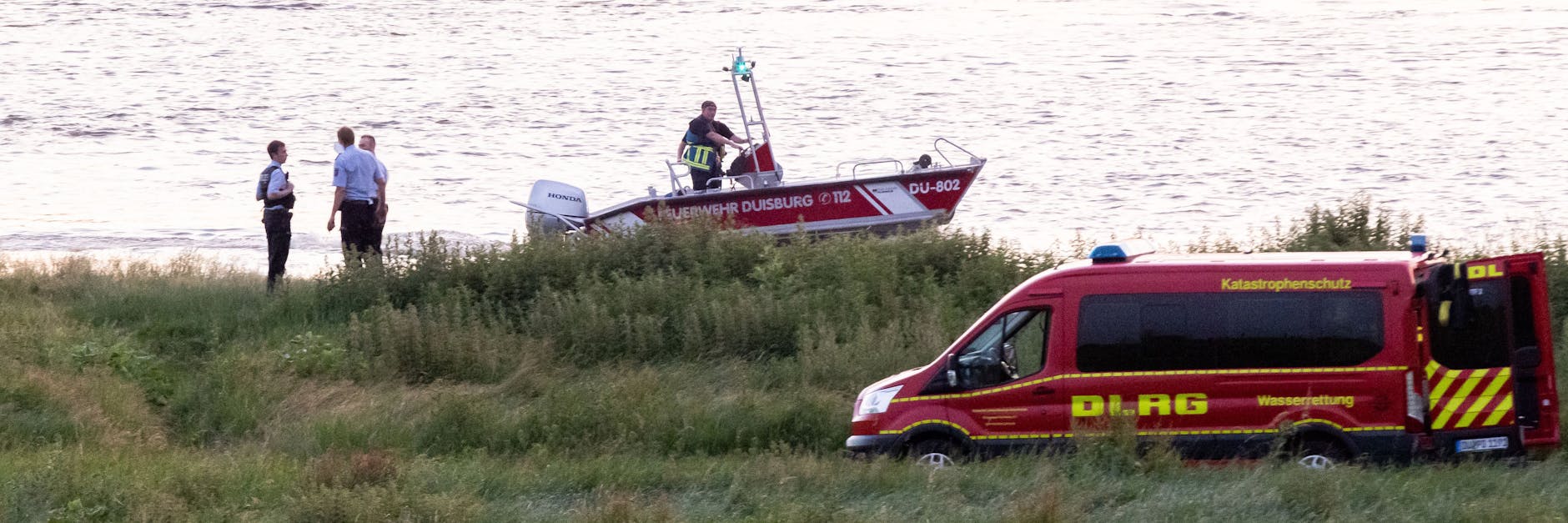 Einsatzkräfte der Polizei, Feuerwehr und DRLG arbeiten am Ufer des Rheins. 
