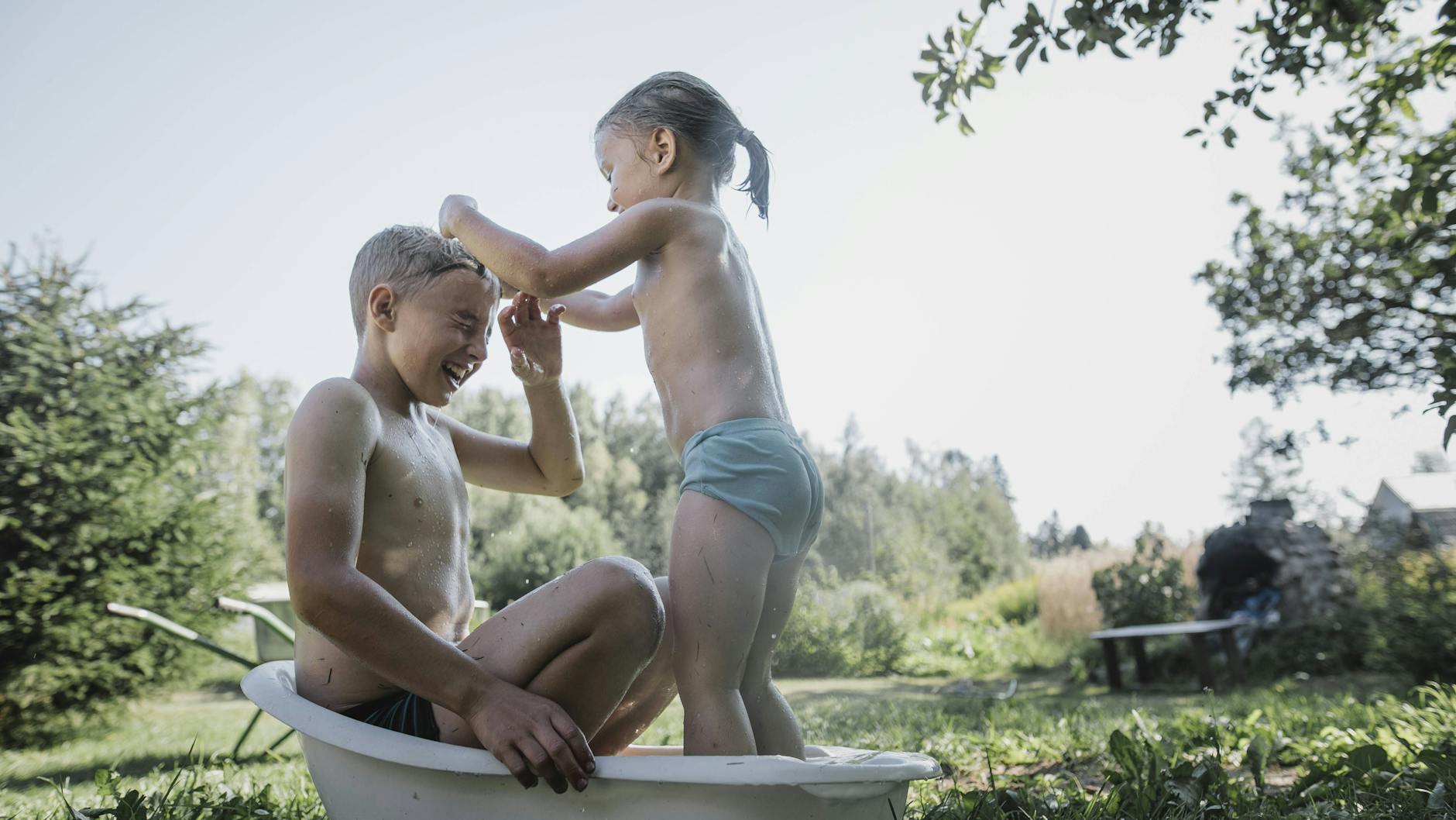 Geschwister spielen in einer Badewanne im Garten.