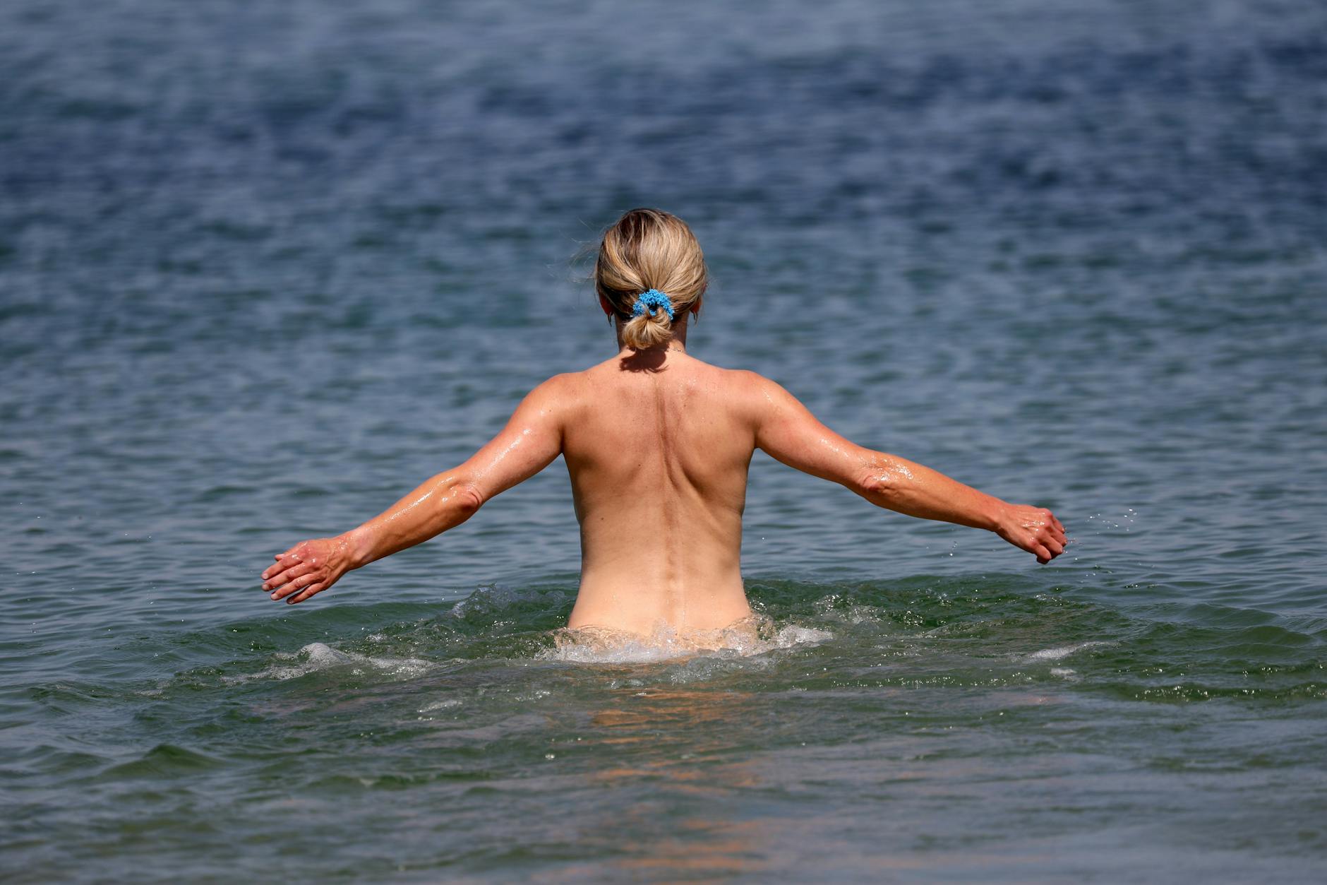 Eine Frau geht an einem FKK-Abschnitt des Ostseebades Warnemünde ins Wasser.