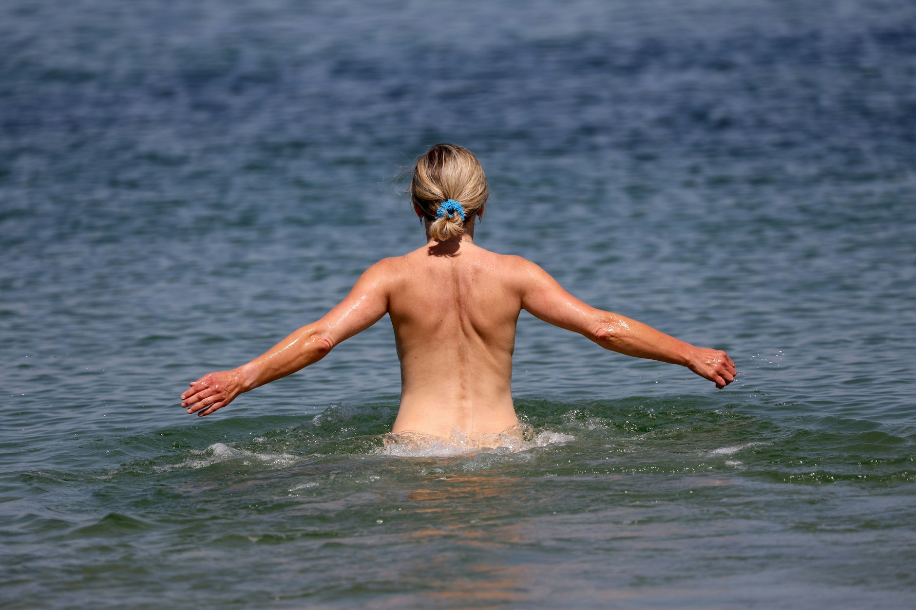 Eine Frau geht an einem FKK-Abschnitt des Ostseebades Warnemünde ins Wasser.