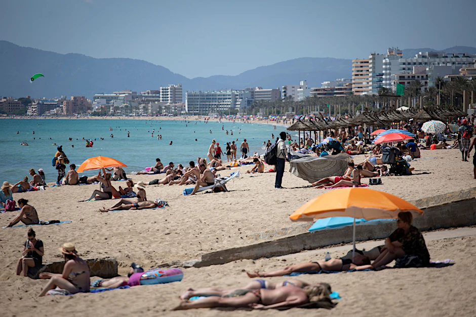 Touristen genießen die Sonne an einem Strand auf Mallorca. Bei Klassenfahrten auf die Insel haben sich mehrere Hundert Schüler mit Corona infiziert.