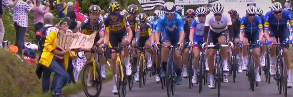 Die Frau im gelben Regenmantel hielt ein Pappschild mit der Aufschrift „Allez Opi-Omi“ in die Motorrad-Kameras – und löste damit einen Massensturz der Tour-Fahrer aus.