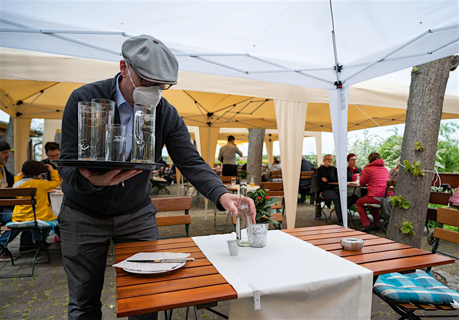 Wirt Mario Kade räumt auf der Terrasse seines „Restaurants am Pfingstberg“ einen Tisch ab. Die anhaltende Corona-Testpflicht stellt viele seiner Kollegen vor die Frage: Mache ich jetzt auf oder nicht? Denn noch immer kommen wenig Gäste.