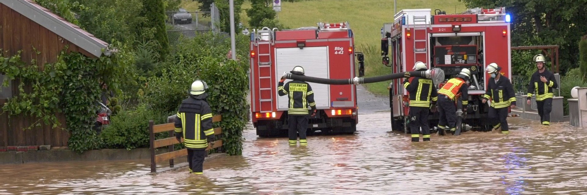 Einsatzkräfte der Feuerwehr stehen auf einer durch ein Unwetter überfluteten Straße.