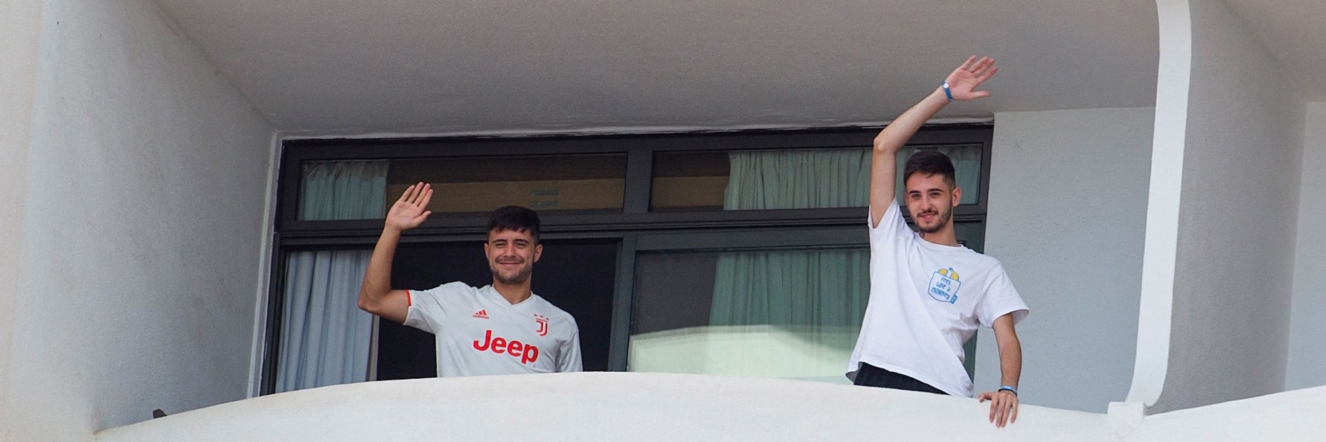 Zwei der Schüler in Zwangs-Quarantäne winken von dem Balkon des Hotels, in dem sie untergebracht sind.